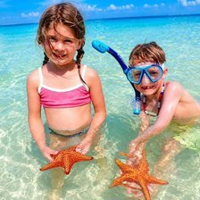 Cayman Adventure Tours family friendly tour - two young children in snorkel masks holding starfish in knee-deep clear water at Starfish Point in Grand Cayman